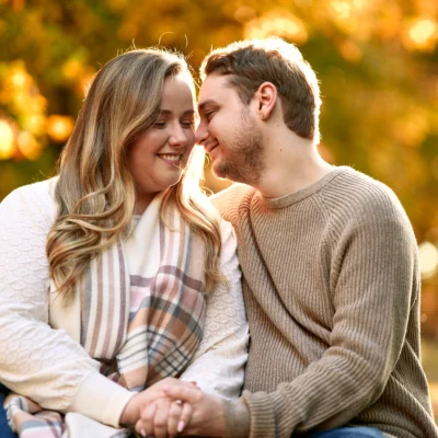 Guy and girl sitting with trees behind them in fall Scotsdale Farm Engagement Photoshoot